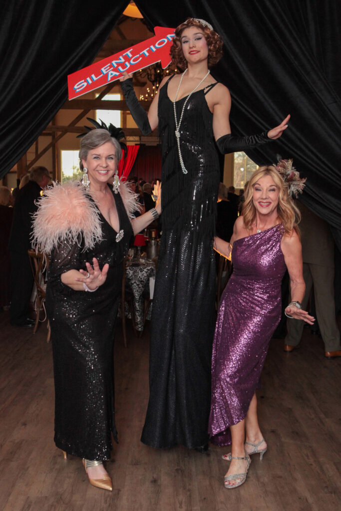 Co-Chairs Joan Herring & Wendy Burks with performer on stilts